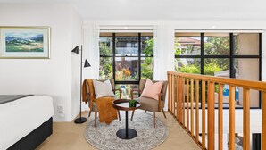 A modern room with a bed, two chairs, a small round table, and a view of the outdoors through large windows. - Balmain Retreat - 2BR + Study (Inner West Council)