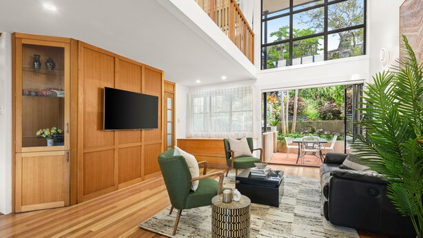 A spacious living area with wooden paneling, a flat-screen TV, green armchairs, a black sofa, and a large window offering a view of the outdoors. - Balmain Retreat - 2BR + Study (Inner West Council)