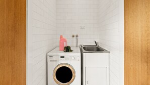 A compact laundry room with a front-loading washing machine, a small sink, and a cabinet. - Balmain Retreat - 2BR + Study (Inner West Council)