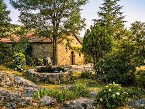 A stone building with a tiled roof, a fountain, and a well-maintained garden with rocks and plants.