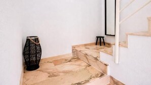 Een trap met marmeren treden, een zwarte decoratieve vaas, een klein krukje en een spiegel aan de muur.