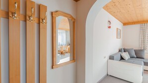 A room with a wooden ceiling, a white sofa, a mirror, and a wooden door with three handles. - Beautiful apartment for 4 people with TV and balcony (Neukirchen Am Großvenediger)