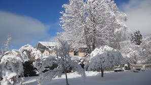 A snow-covered landscape with a large tree in the foreground and a building in the background. - Beautiful apartment for 4 people with TV and balcony (Neukirchen Am Großvenediger)