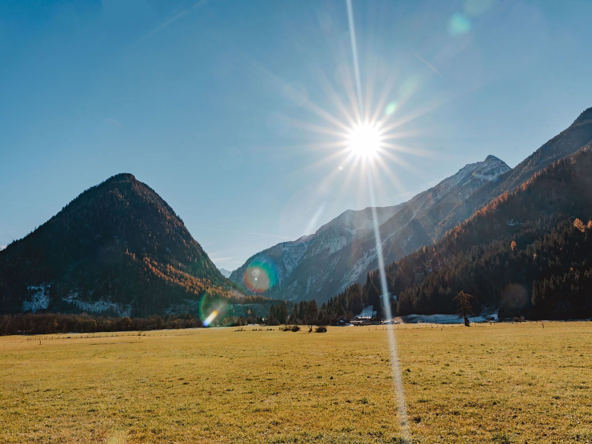 A wide-open field with mountains in the background and a bright sun shining in the sky.