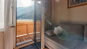 Una habitación con puerta corrediza de vidrio que da a una terraza de madera con vista a la montaña.