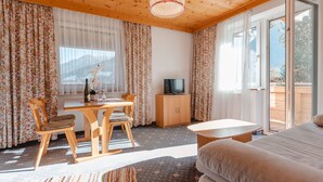 Una habitación acogedora con techo de madera, una mesa de comedor con sillas, un sofá, un televisor y un gran ventanal corredera al exterior.