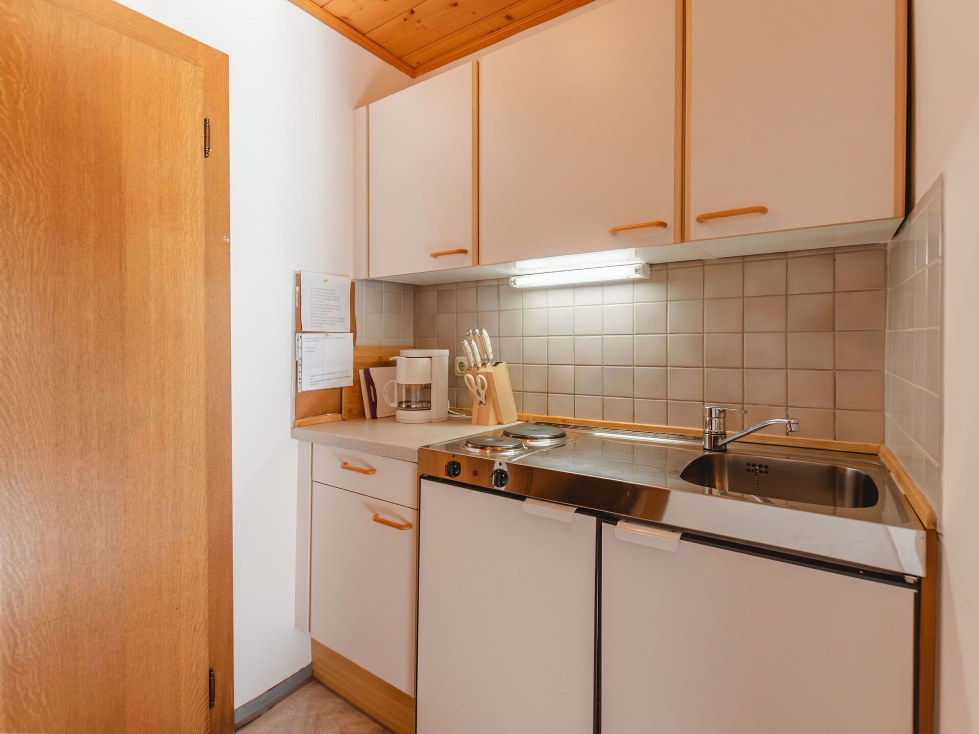 Een kleine keuken met witte kasten, een roestvrijstalen spoelbak en een koffiezetapparaat.
