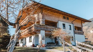 Una casa de madera de dos pisos con un balcón, rodeada de árboles y un cielo despejado.