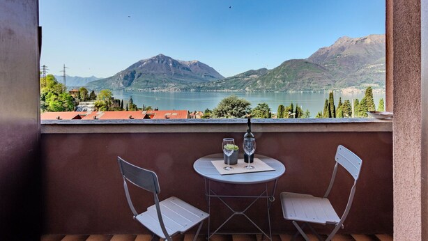 Un balcon avec deux chaises et une table, donnant sur un lac et des montagnes.