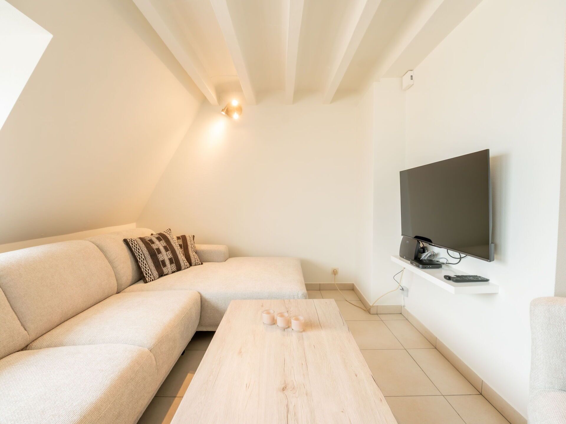 Un salon moderne avec un canapé, une table basse et un téléviseur à écran plat fixé au mur.