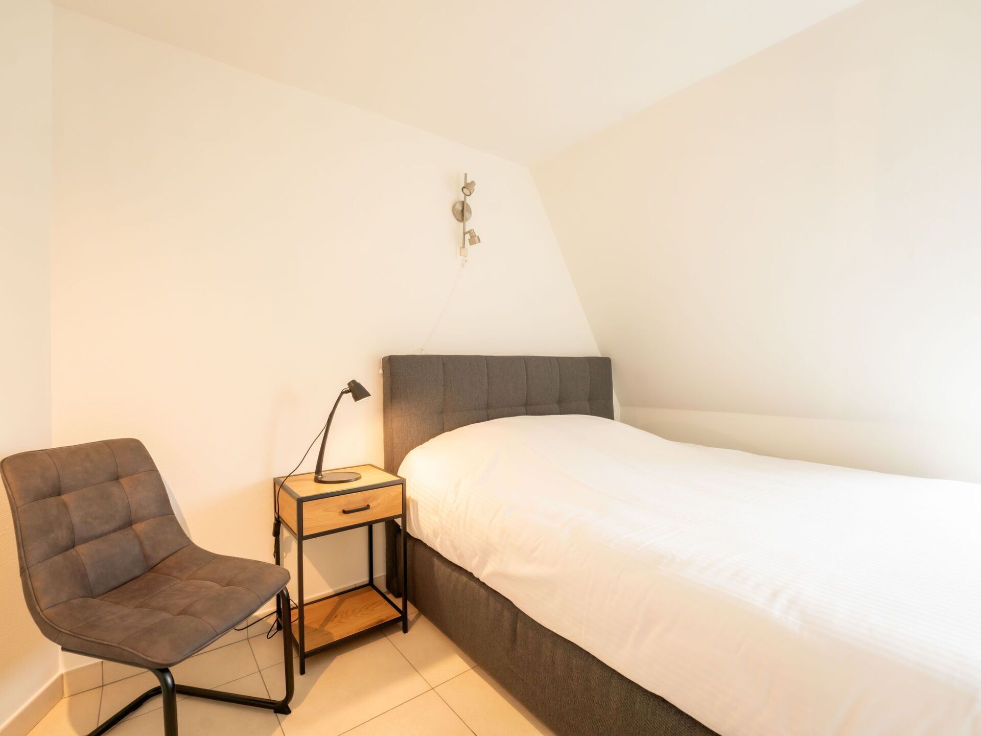 Une chambre avec un lit simple, une table de chevet avec une lampe et une chaise.