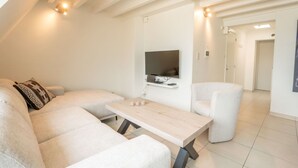 A modern living room with a sofa, a coffee table, and a TV mounted on the wall. - Lovely apartment for 4 guests with WIFI and TV (De Haan)