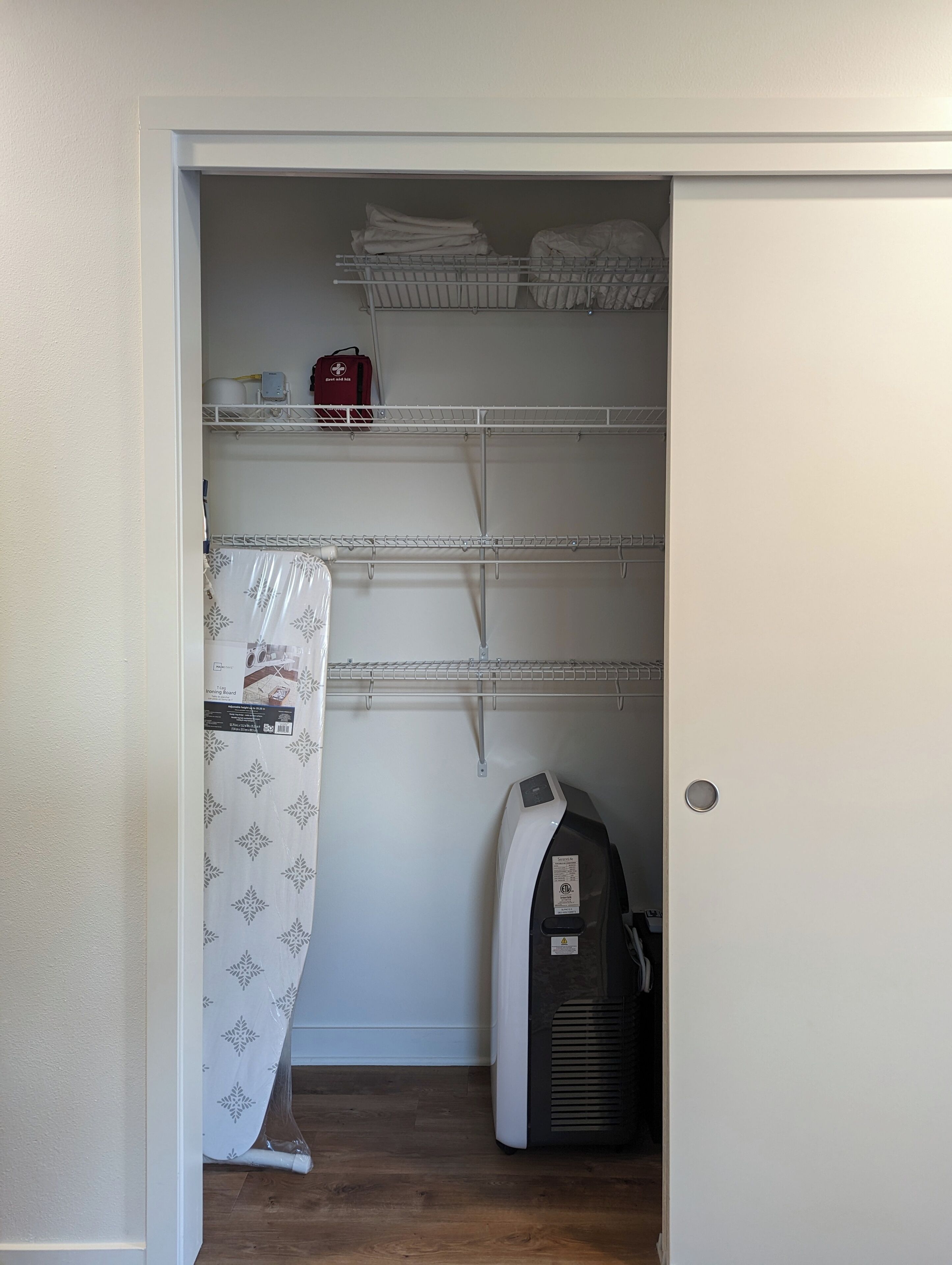 Une buanderie équipée d’un lave-linge, d’un sèche-linge et d’étagères où sont pliés des vêtements, ainsi qu’un sac rouge.