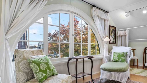 A cozy room with a large arched window, a wicker chair, a cushioned bench, and a small table. - Enjoy this comfortably furnished, historic Craftsman home just 1 block from downtown McMinnville (McMinnville)