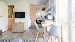 Et kompakt køkken med moderne hårde hvidevarer, et spiseområde med to stole og et TV ophængt på væggen.