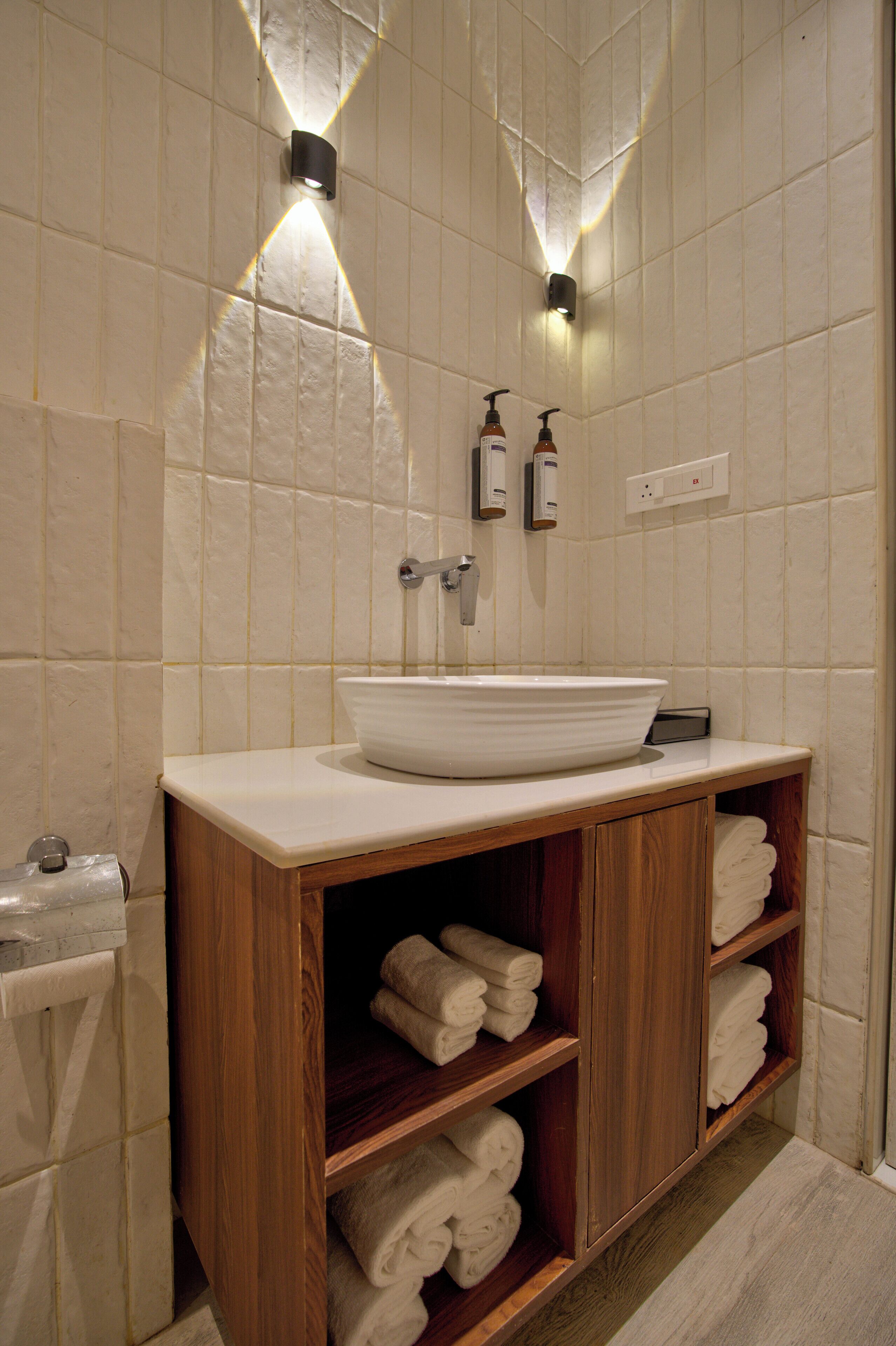 A bathroom with a wooden vanity, a white sink, and shelves with folded towels.