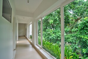 A corridor with large windows offering a view of lush greenery. - Asgard Apartments & Hotels (Siolim)