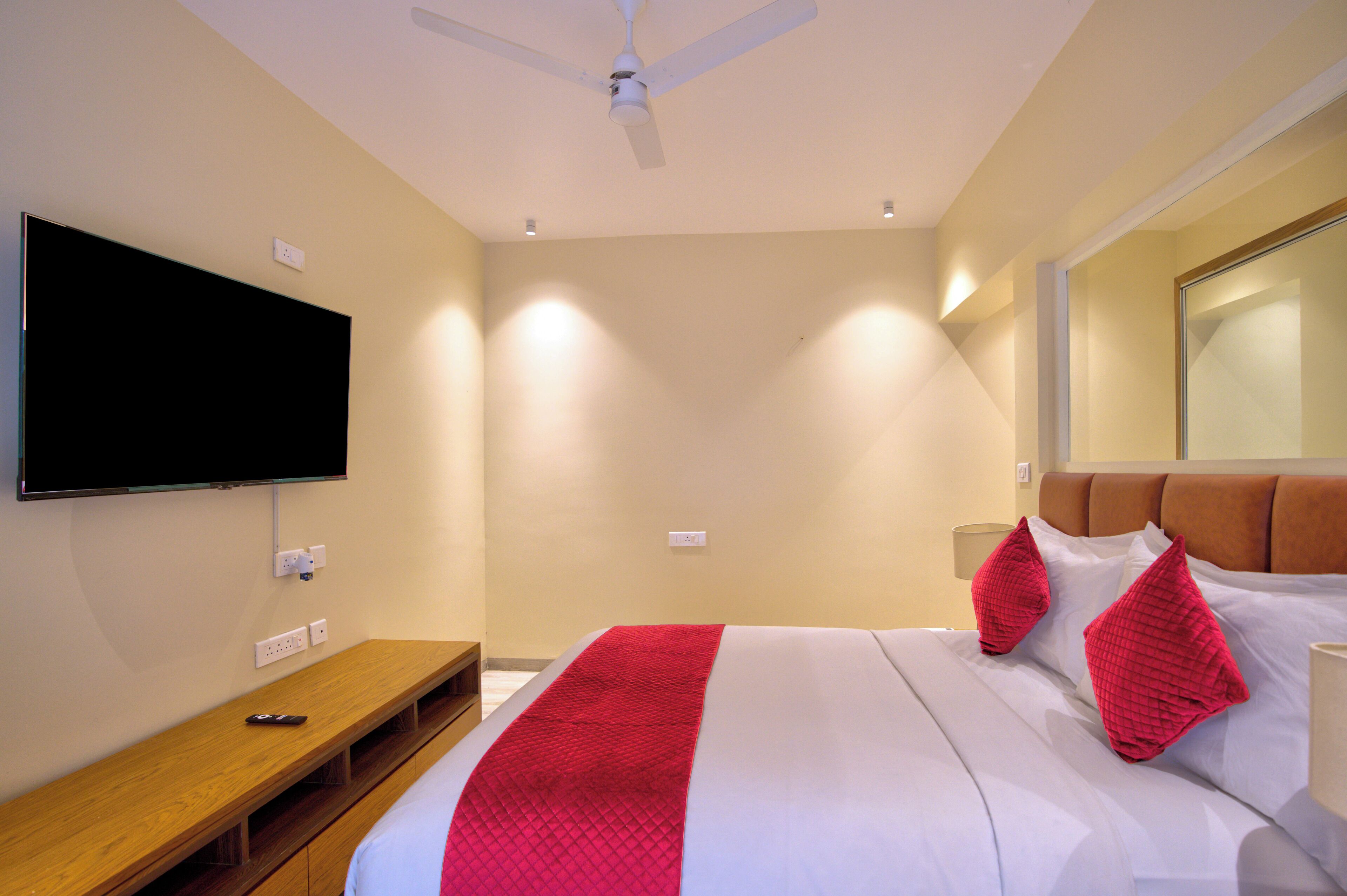 Ein Hotelzimmer mit einem Bett, einem an der Wand befestigten Fernseher, einem Deckenventilator und einem Nachttisch.