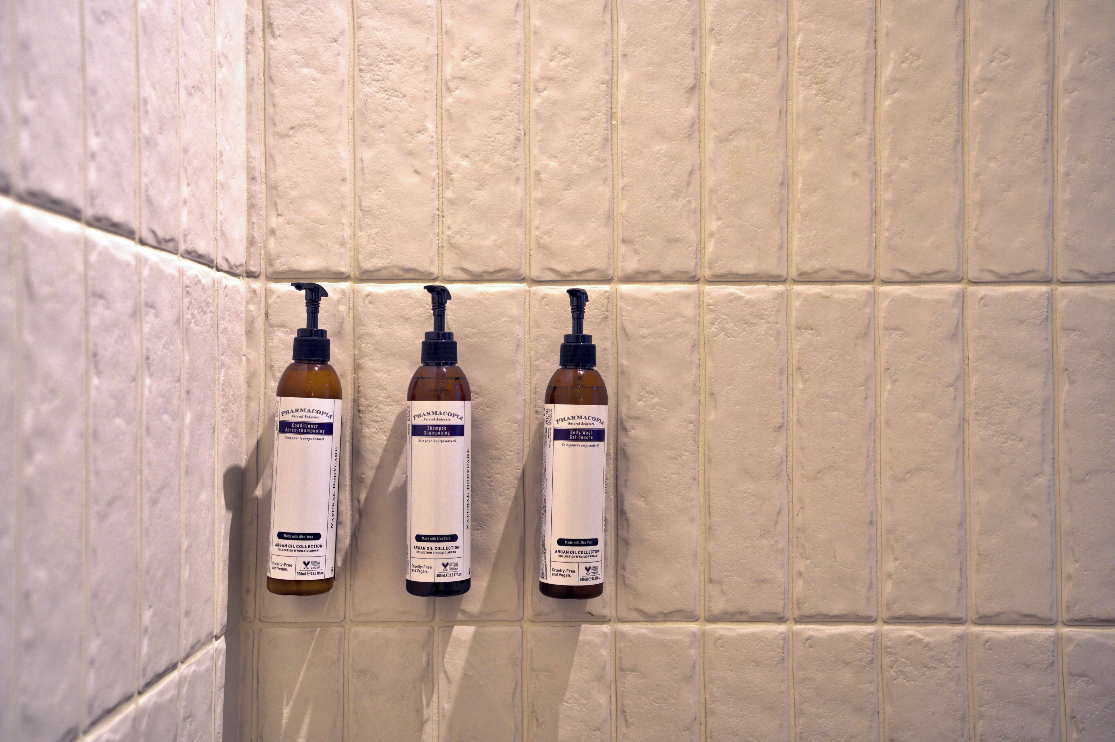 Trois flacons de gel hydroalcoolique fixés à un mur recouvert de carreaux.