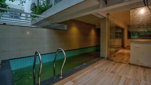 Ein moderner, überdachter Schwimmbereich mit Glaswänden, einer Holzterrasse und einem Metallgeländer.