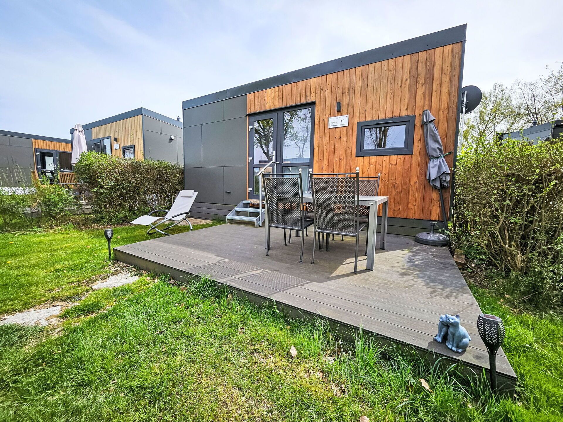 A modern building with a wooden facade, a patio with chairs and a table, and a small garden area.