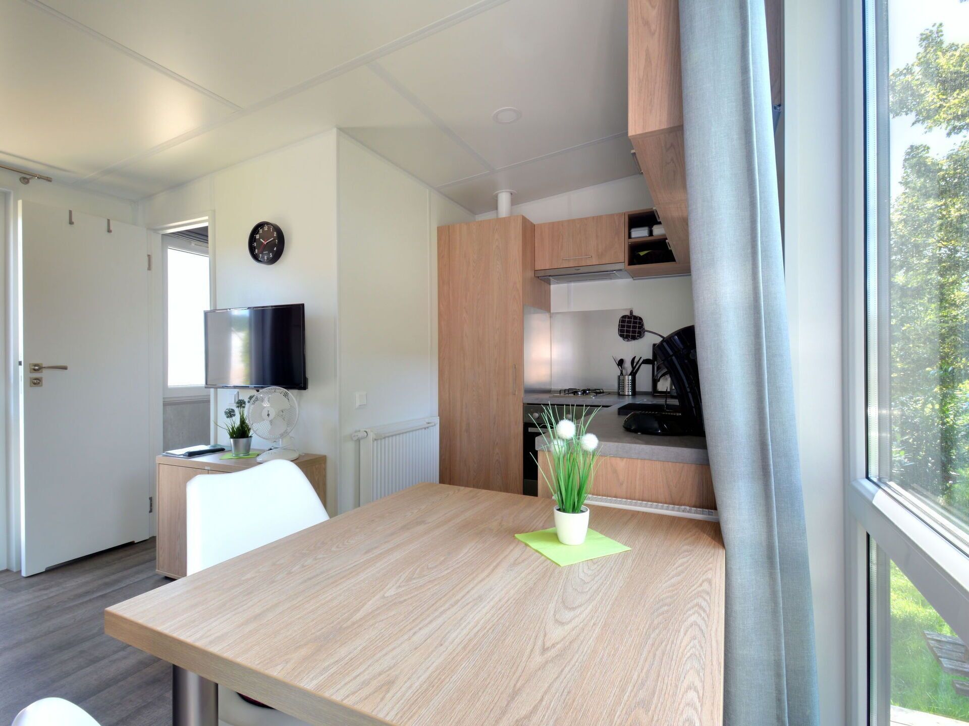 Une cuisine moderne avec des meubles en bois, une cuisinière encastrée et une fenêtre donnant sur un paysage verdoyant.