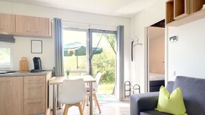 A modern kitchen with wooden cabinets, a dining table with chairs, a grey sofa with a green pillow, and a sliding glass door leading to an outdoor area. - Nice apartment in villa for 4 guests with WIFI, TV and terrace (Beilngries)