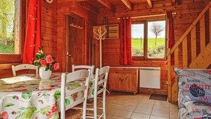 A wooden cabin interior with a dining table, chairs, a vase of flowers, a clock, and a window with a view of a green field. - Beautiful private villa for 5 guests with TV, terrace and pets allowed (Camps-saint-mathurin-léobazel)