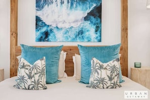 A bedroom with a large ocean wave painting, two matching pillows, and a wooden headboard.