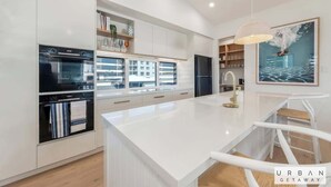 Una cocina moderna con armarios blancos, una isla central y un comedor con una silla blanca.