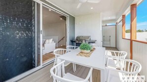 A modern outdoor dining area with a white table and chairs, a ceiling fan, and a grill in the background.