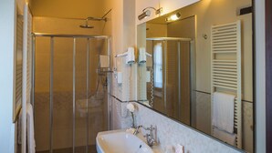A bathroom with a glass shower enclosure, a sink with a mirror, and a towel rack. - Deluxe Double Room (DERUTA)