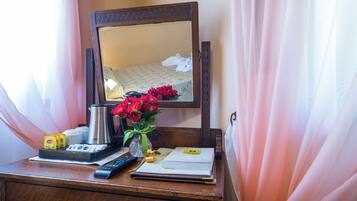 A wooden desk with a remote control, a coffee pot, a vase with flowers, and a book.