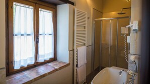 A bathroom with a shower, a sink, and a window with curtains. - Deluxe Double Room (DERUTA)
