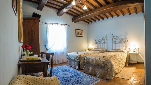 A bedroom with two beds, a wooden ceiling, a desk with a chair, and a window with curtains. - Deluxe Double Room (DERUTA)