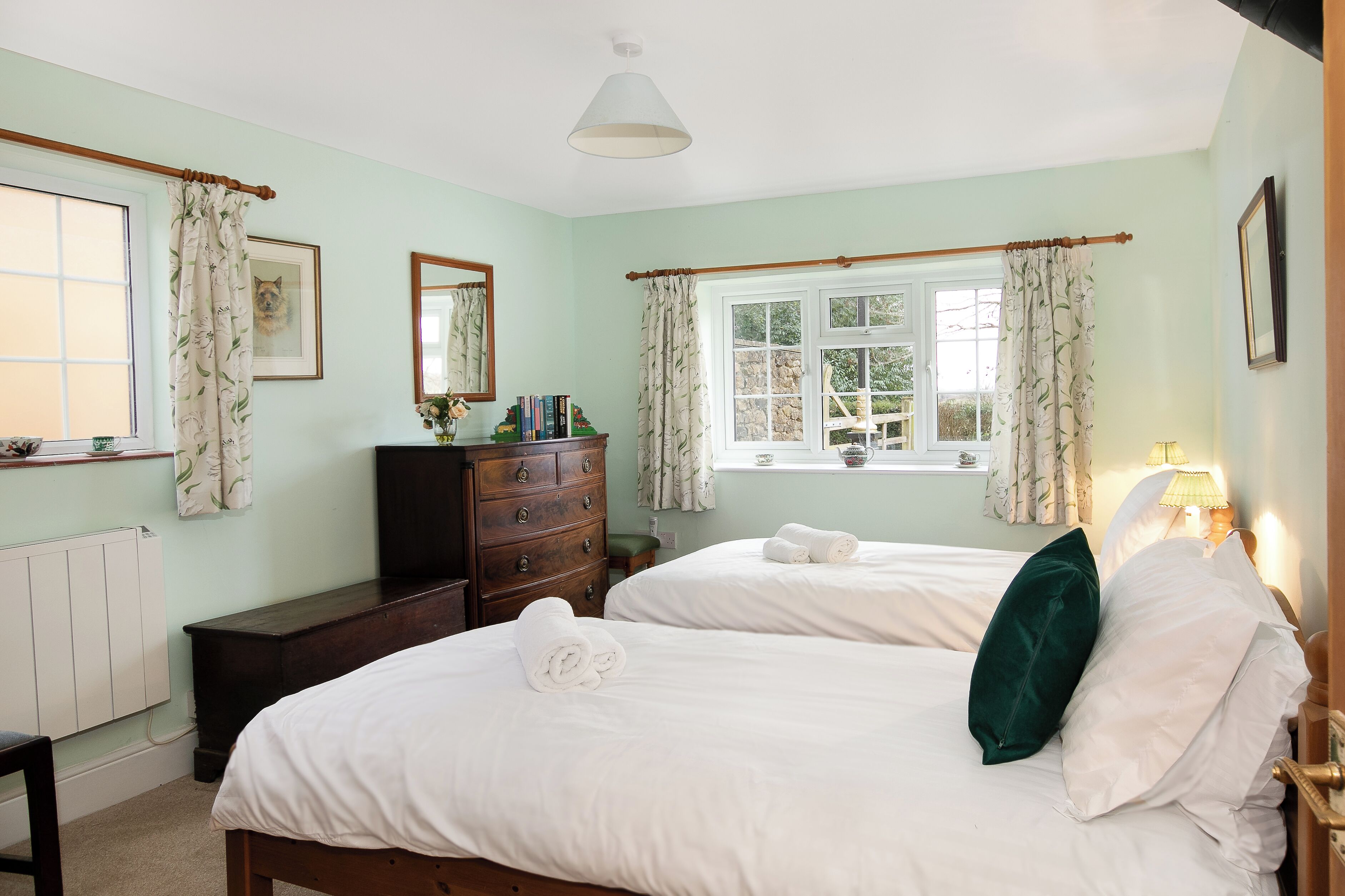 Une chambre avec deux lits, une commode, un miroir et une fenêtre avec des rideaux.