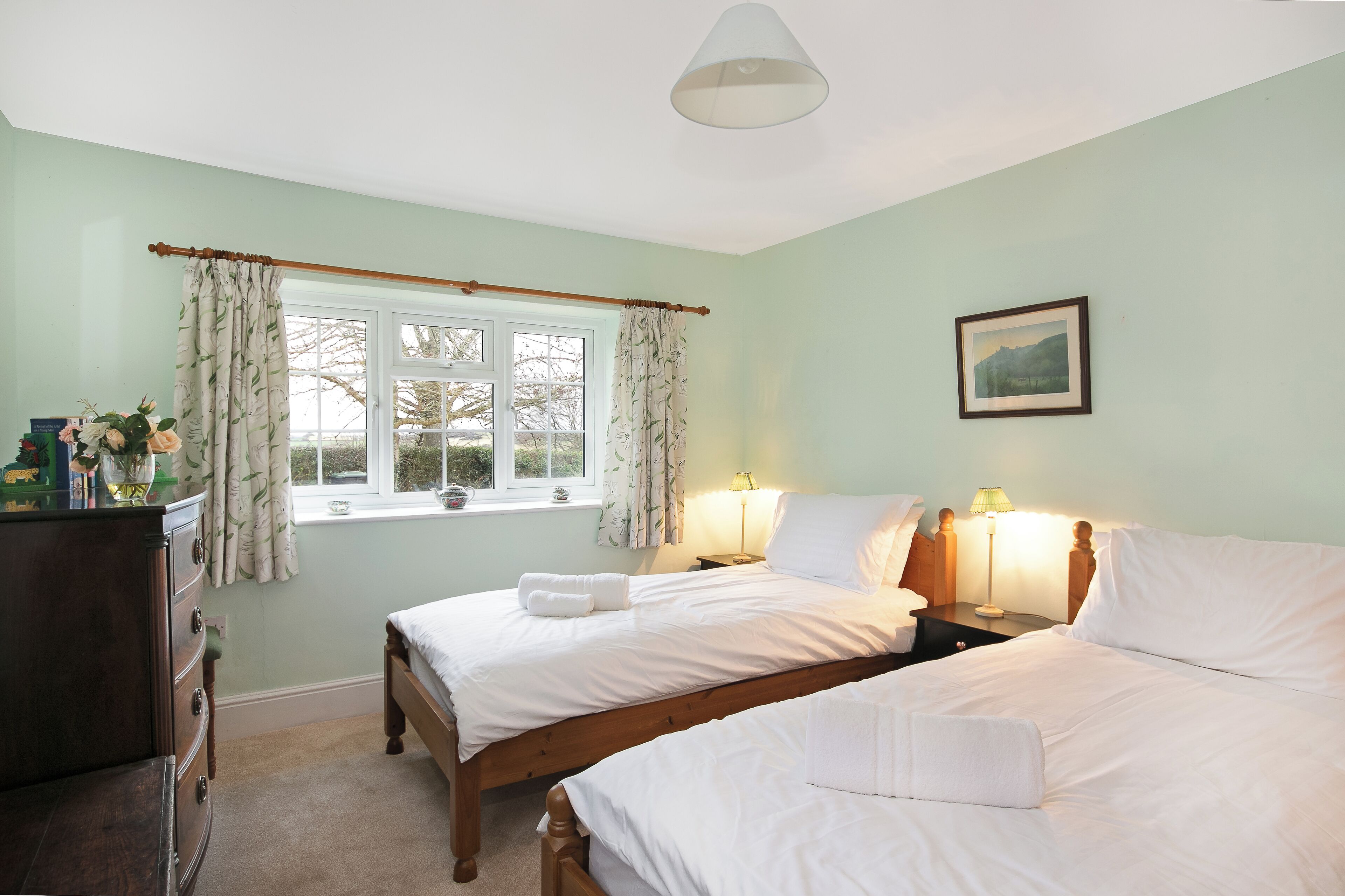 A bedroom with two beds, a dresser, a window with curtains, and a framed picture on the wall.