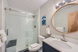 Enjoy a refreshing shower in the bathroom, featuring a glass-enclosed shower, white toilet, and oval sink with a sleek faucet.