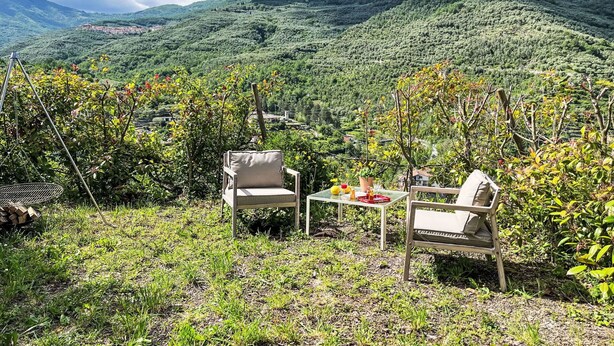 Eine Terrasse mit zwei Stühlen und einem Tisch, mit Blick auf ein üppiges Tal und ferne Hügel.