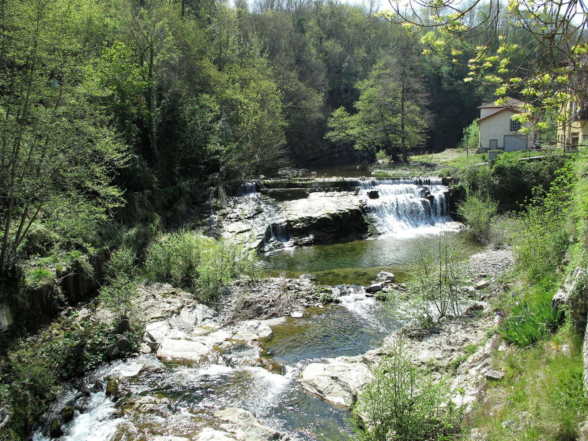 A natural landscape with a waterfall, rocky terrain, and dense greenery.