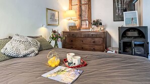 Ein gemütliches Schlafzimmer mit einem Bett, einer Holzkommode, einer Lampe, einem gerahmten Bild und einem Kamin.