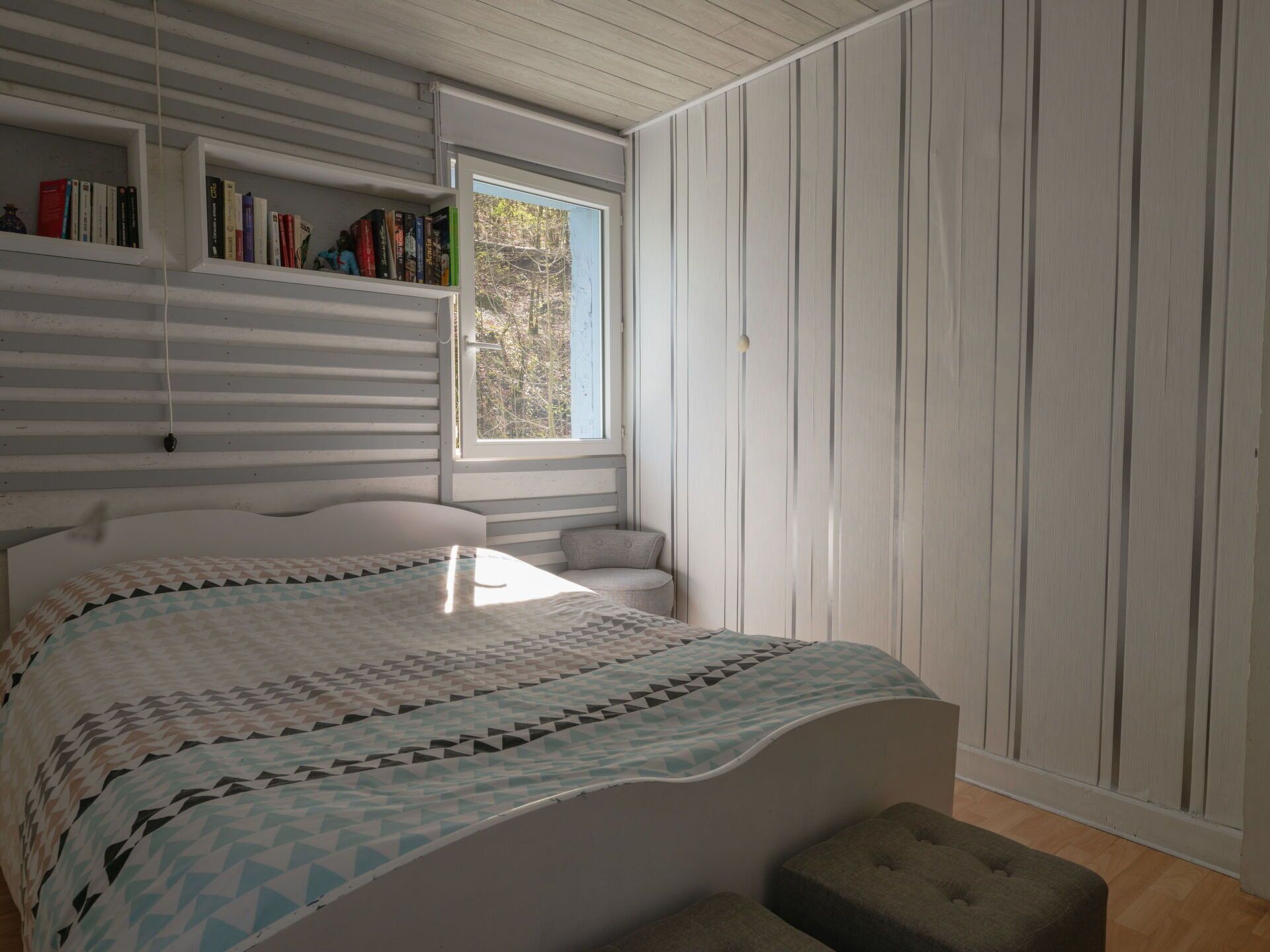A bedroom with a bed, a window, and a bookshelf.