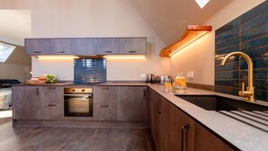A modern kitchen with dark wood cabinets, a built-in oven, and a large island with a sink and a gold faucet. - Beautiful private villa for 6 people with WIFI, TV and pets allowed (Newquay)