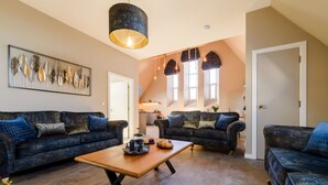 A spacious living area with two dark blue sofas, a wooden coffee table, and a large pendant light. - Beautiful private villa for 6 people with WIFI, TV and pets allowed (Newquay)