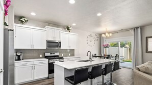 A modern kitchen with white cabinets, a central island with bar stools, a microwave, and a stove.