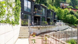 A modern multi-story building with balconies, surrounded by lush greenery and a stone retaining wall. - Nice apartment for 3 people with WIFI, A/C, pool, TV and terrace (Nesso)