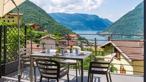 A terrace with a table set for dining, overlooking a lake and mountains. - Nice apartment for 3 people with WIFI, A/C, pool, TV and terrace (Nesso)