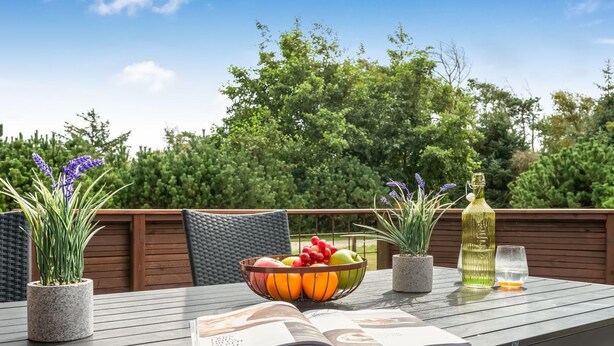 Een patio tafel met een fruitschaal, een fles olijfolie, een glas en een open tijdschrift.