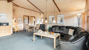 Een knus kamer in chaletstijl met een houten plafond, een zwarte leren bank, een houten eettafel en een klein keukenhoekje.