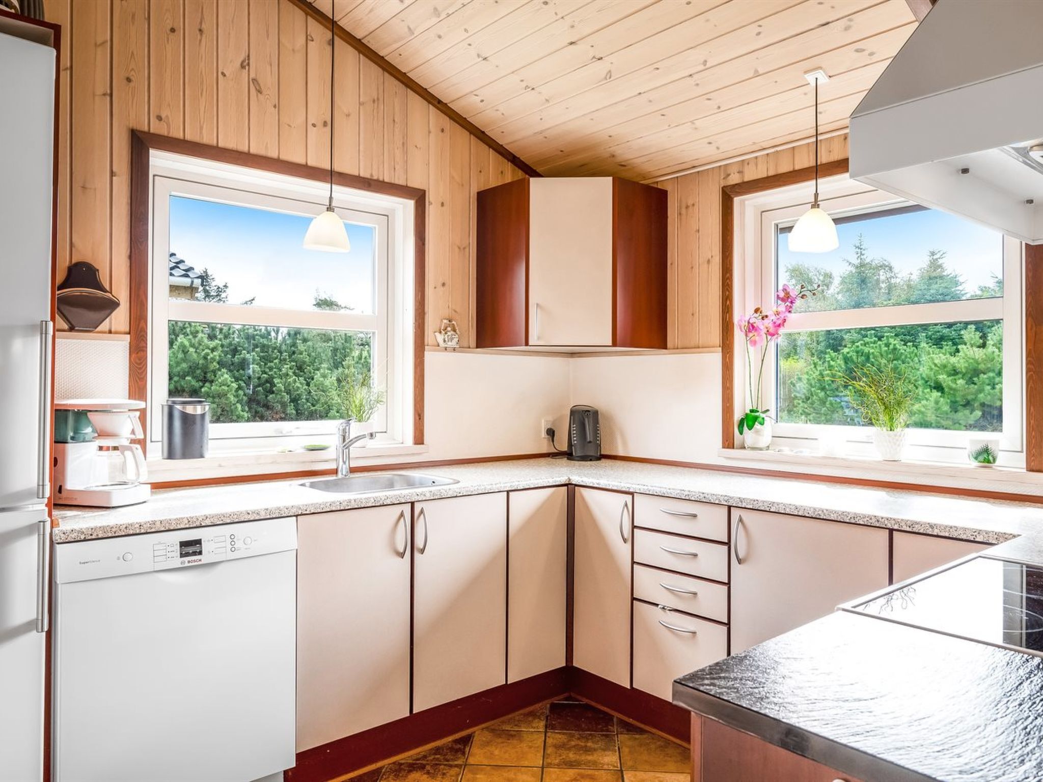 A modern kitchen with wooden cabinets, a built-in dishwasher, and a window with a view of greenery.